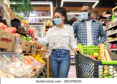 Family Grocery Shopping. Black Couple Buying Vegetables And Fruits Together Standing With Shop Trolley Cart In Supermarket Groceries Store, Wearing Surgical Mask. Customers Choosing Healthy Food.