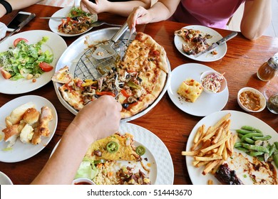 Family Group Hand Eating Big Meal With Pizza , Rib Steak ,taco And Salad On Wooden Table Background, Dinner Celebrate.