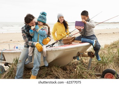 Family Group Sitting On Boat With Fishing Rod On Winter Beach