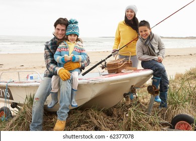 Family Group Sitting On Boat With Fishing Rod On Winter Beach