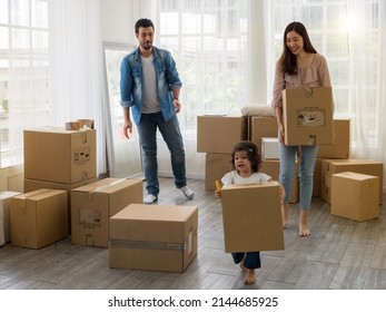Family happily helping carrying cardboard boxes when moving house. Father, mother enjoying looking at adorable toddler daughter helping carrying box.