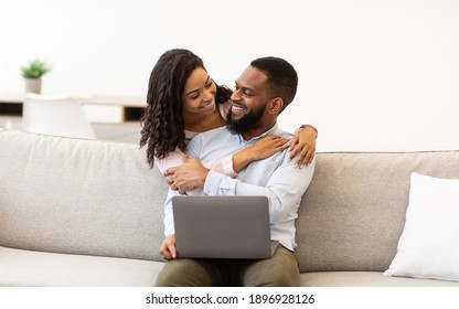 Family Happiness. Cheerful Black Couple Web Surfing On Laptop Together, Sitting On Sofa At Home, Relaxing And Hugging, Copy Space. Smiling Young African American Woman Embracing Man From Behind