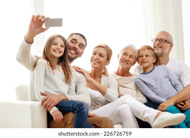 family, happiness, generation and people concept - happy family sitting on couch and making selfie with smartphone at home - Powered by Shutterstock