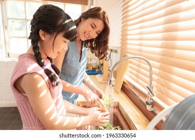 Family Happy Asian Mother And Daughter Washing Vegetables Together At Kitchen.