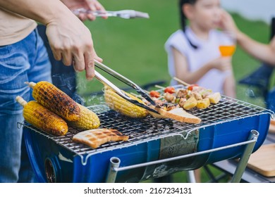 Family Happy Meal Outdoors Backyard Party BBQ Grilled. Roasted Meat And Corn Bread Cooking At Barbecue Stove Closeup.