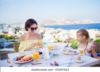 Family Having Breakfast At Outdoor Cafe With Amazing View On Mykonos Town. Adorable Girl And Mom Drinking Fresh Juice And Eating Croissant On Luxury Hotel Terrace