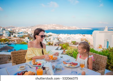 Family Having Breakfast At Outdoor Cafe With Amazing View On Mykonos Town. Adorable Girl And Mom Drinking Fresh Juice And Eating Croissant On Luxury Hotel Terrace