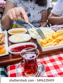 Family Having Delicious Rich Traditional Turkish Breakfast Include Tomatoes, Cucumbers, Cheese, Butter, Eggs, Honey, Bread, Olives, Jam, Sausage, Fried Potatoes And Tea Cups. 