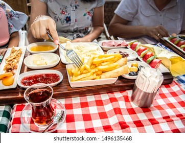 Family Having Delicious Rich Traditional Turkish Breakfast Include Tomatoes, Cucumbers, Cheese, Butter, Eggs, Honey, Bread, Olives, Jam, Sausage, Fried Potatoes And Tea Cups. 