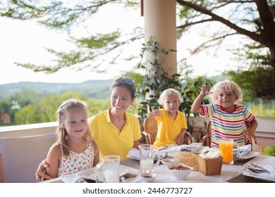 Family having dinner on outdoor patio. Mother and kids eating breakfast or lunch on a rooftop terrace in tropical resort. Garden and backyard dining area. Children eat outdoors. - Powered by Shutterstock