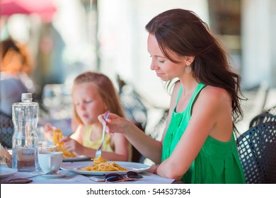 Family Having Dinner At Outdoor Cafe With Italian Menu. Adorable Girl And Mother Eating Spaghetti On Luxury Hotel Terrace