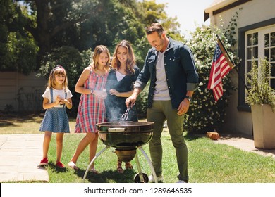 Family having fun cooking food together in their backyard. Man making barbeque standing in their backyard with wife and kids.