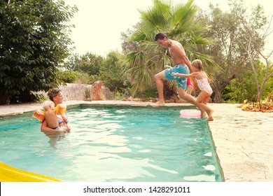 Family Having Fun In Holiday Villa Swimming Pool Garden, Swimming And Jumping Into The Water On Summer Vacation Outdoors. Adults And Children Enjoying Fun Games Play Leisure Recreation Lifestyle.