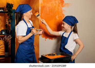 Family Having Fun With Orange Paint, Using Color To Renovate Apartment Walls Together. Woman With Child Laughing And Painting House Room With Paintbrush Tools And, Diy Interior Job.