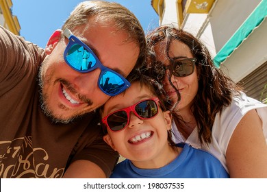 Family having fun wearing sunglasses & waving to a camera taking selfie photograph on summer holiday - Powered by Shutterstock