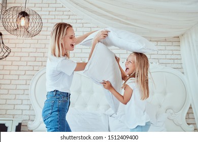 Family Having Funny Pillow Fight On Bed. Beautiful Mom With Her Little Cute Daughter Spending Free Time Together