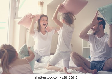 Family having funny pillow fight on bed. Parents spending free time with their daughters.  - Powered by Shutterstock