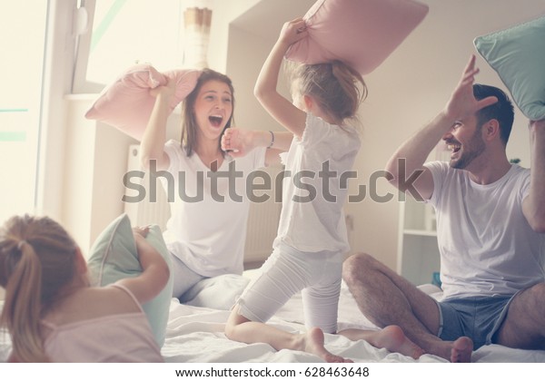 Family having funny pillow fight on\
bed. Parents spending free time with their daughters.\
