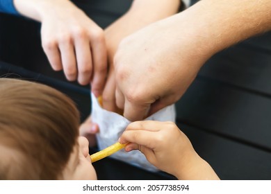 The Family Is Having Lunch At A Fast Food Cafe. The Family Eats French Fries Together. Children's Hands Grab Pieces Of Fried Potatoes. Friends Eat French Fries.  Photo Of People Sharing Potatoes.