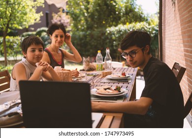 Family Having Lunch Outdoors In Their Home Garden While Watching A Movie With Laptop. Real Lifestyle.