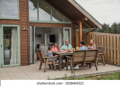 Family Having Their Breakfast Outside The Holiday Cottage.