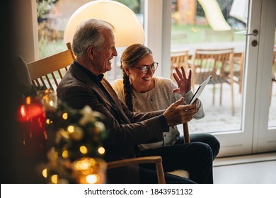 Family having a video call on table pc during christmas. Senior couple greeting family during a video call on a Christmas eve.