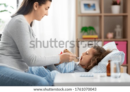 family, health and medicine concept - mother giving cough syrup to little sick daughter lying in bed at home