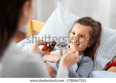 family, health and medicine concept - mother pouring cough syrup for little sick daughter lying in bed at home