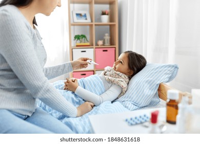 Family, Health And People Concept - Mother With Thermometer Measuring Temperature Of Sick Daughter Lying In Bed At Home