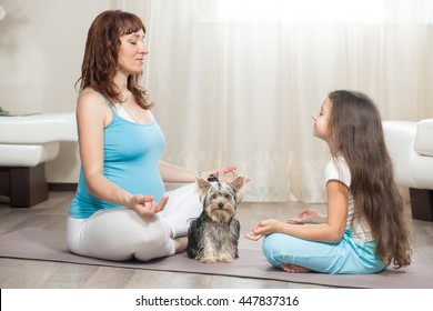 Family healthy lifestyle concept. Pregnancy Yoga and Fitness. Young pregnant mom practicing yoga with her dog and happy kid girl in living room. Pregnant mother and child meditating together at home - Powered by Shutterstock