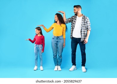 Family Hierarchy. Arabic Parents And Daughter Posing Together Measuring Each Other's Height With Hand Standing Over Blue Background. Studio Shot, Full Length