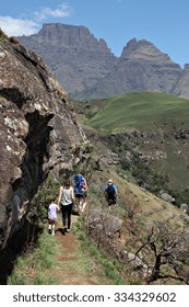 A Family Of Hikers Make Their Way Along A Narrow Hiking Trail Under Champagne Castle And Cathkin Peak In The Drakensberg Mountain Range In Rural KwaZulu-Natal, South Africa.