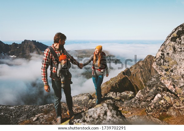 Family hiking man and woman\
traveling with baby carrier outdoor healthy lifestyle vacations in\
mountains mother and father holding hands eco tourism summer\
activity 