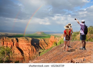 Family Hiking On Vacation, Taking Pictures With Phone And Relaxing On Top Of The Mountain, Looking At Beautiful Rainbow At Sunset , Mountains Landscape. Grand Canyon National Park, Arizona, USA.