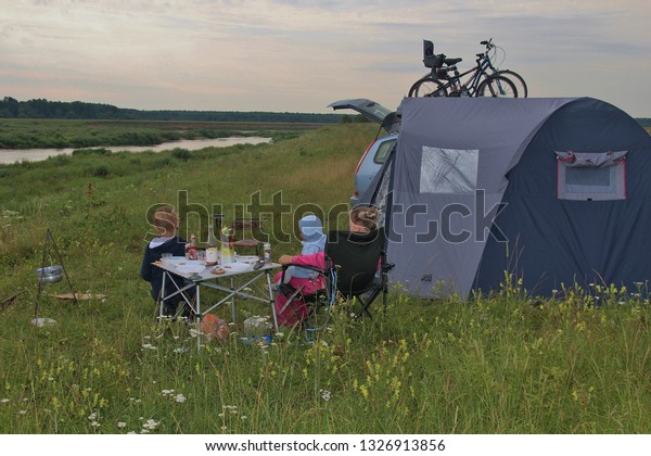 Family hiking with a tent\
in a field near the Volga River. Camping in nature near the forest.\
Tent, car, children and bicycles. Staritsa, Tver region Russia -\
07/2013.