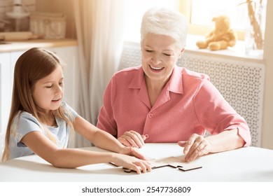 Family hobbies. Elderly woman and her grandchild playing puzzle game together in kitchen - Powered by Shutterstock