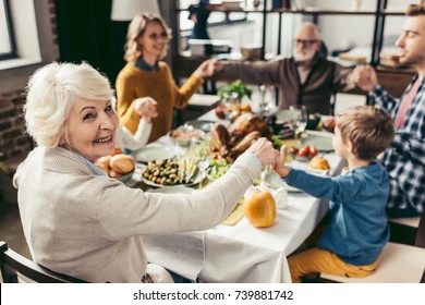 Family Holding Hands And Praying On Thanksgiving Before Holiday Dinner