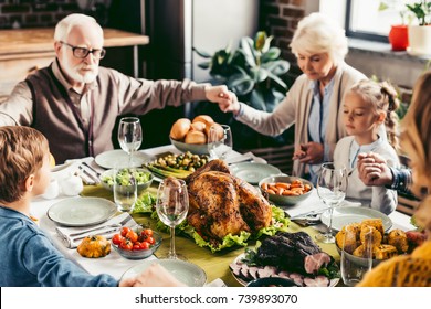 Family Holding Hands And Praying On Thanksgiving Before Holiday Dinner