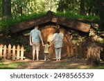 Family holding hands standing in front of a wooden hobbit house door in a forest. Outdoor photography for design and print. Nature and fantasy concept