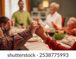 Family holding hands together in prayer around the dinner table at christmas time. They are thankful for their blessings