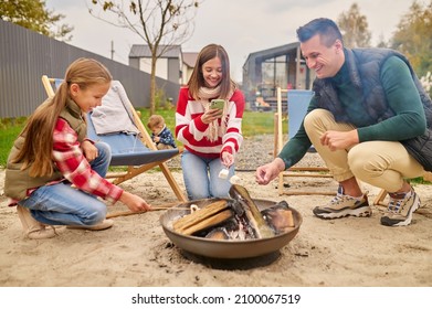 Family Holding Marshllow On Stick Over Campfire In Yard