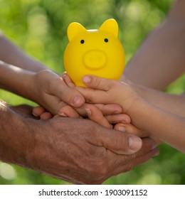 Family Holding Piggy Bank In Hands Against Green Spring Background. Fundraiser For Environmental Protection Concept