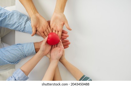 Family holding red heart in hands. Mom, dad and kid feeling united, sharing love, cherishing gift of life, promoting charity, NGO, donation, heart health, healthcare. Top view close up white copyspace