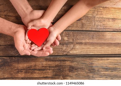 Family Holding Small Red Heart In Hands On Wooden Background