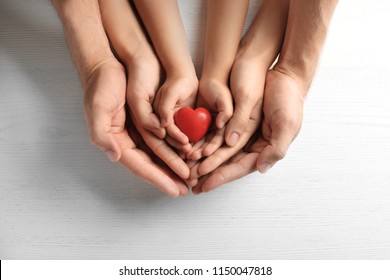 Family holding small red heart in hands on wooden background