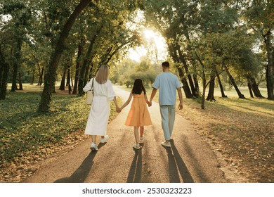 A family holds hands walking along a sunlit path in the park. - Powered by Shutterstock