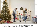 Family holiday funny dance, mother and father with two small kid have fun on Christmas eve together at home celebrate traditional New Year winter holidays, enjoy traditional activity near festive tree