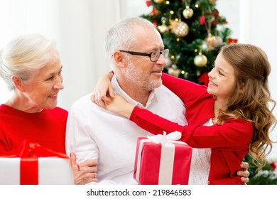 Family, Holidays, Generation, Christmas And People Concept - Smiling Grandparents And Granddaughter With Gift Boxes Sitting On Couch At Home