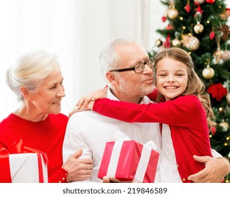 Family, Holidays, Generation, Christmas And People Concept - Smiling Grandparents And Granddaughter With Gift Boxes Sitting On Couch At Home