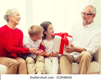 family, holidays, generation, christmas and people concept - smiling grandparents and grandchildren with gift box sitting on couch at home - Shutterstock ID 313948418